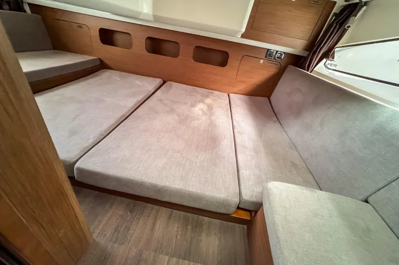 Slide: The Image of 2024 Beneteau Antares 11 interior cabin with gray cushions and wooden accents. - 28