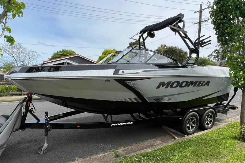 Slide: The Image of 2020 Moomba Max boat on trailer, parked on street, surrounded by greenery. - 2