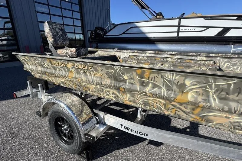 Slide: The Image of 2026 War Eagle 648LDV camo boat on Wesco trailer, parked outdoors. - 8