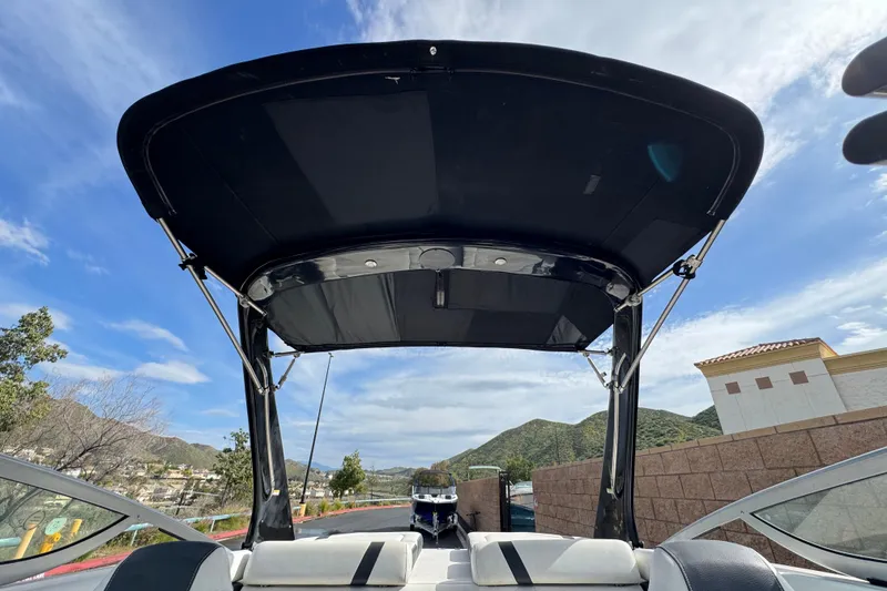 Slide: The Image of 2018 Regal 2100 Bowrider boat with black canopy, scenic mountain backdrop. - 11