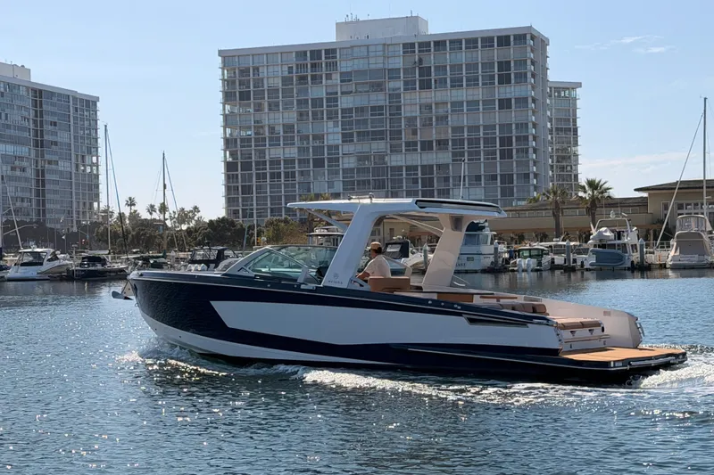 Slide: The Image of 2022 Aviara AV32 I/O boat cruising in a marina with modern buildings in the background. - 2