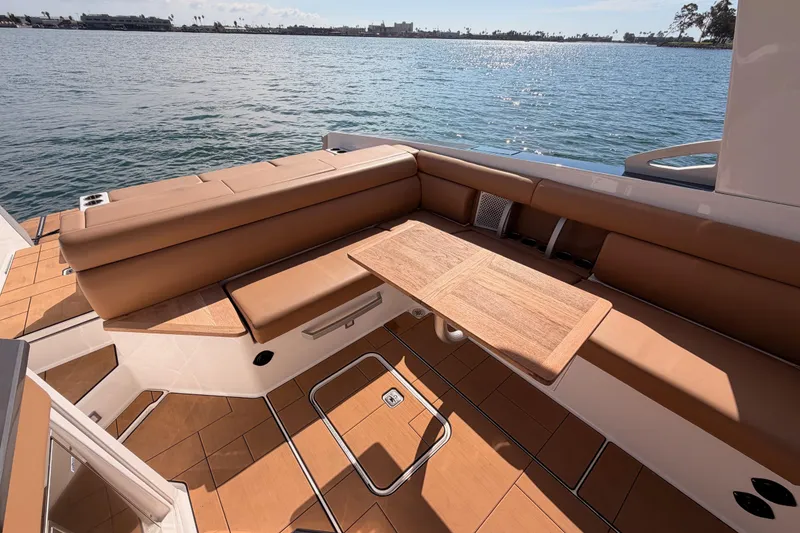 Slide: The Image of 2022 Aviara AV32 I/O boat interior with tan seating and wooden table, overlooking serene water. - 23