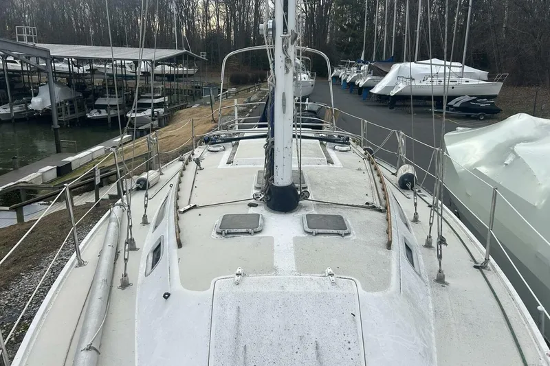 Slide: The Image of 1985 Catalina 36 sailboat docked, surrounded by covered boats and trees in a marina. - 48