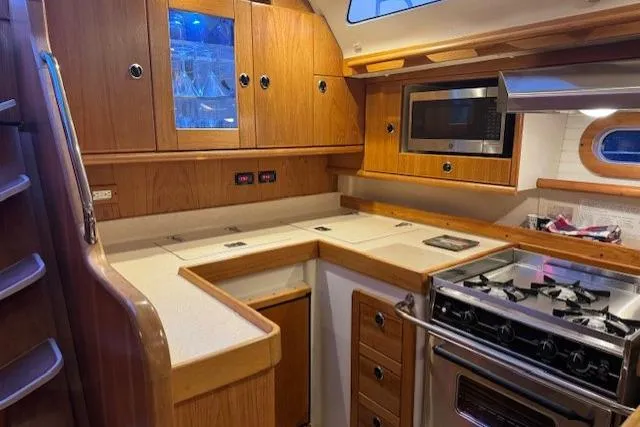 Slide: The Image of 1999 Catalina 470 yacht kitchen with wooden cabinetry, stove, microwave, and countertop. - 70