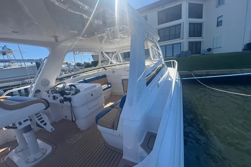 Slide: The Image of 2012 Intrepid 390 Sport Yacht docked, showcasing sleek interior and helm under bright sunlight. - 49