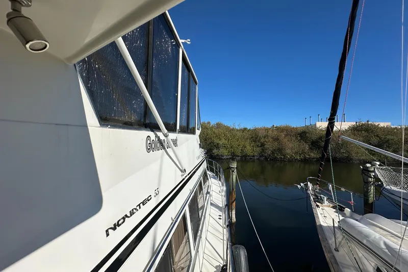 Slide: The Image of 2006 Novatec Islander 55 yacht docked by a serene waterway under clear blue skies. - 8