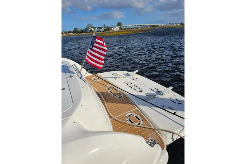 Slide: The Image of 2006 Sea Ray 580 Sedan Bridge yacht with American flag on deck, near shoreline. - 20