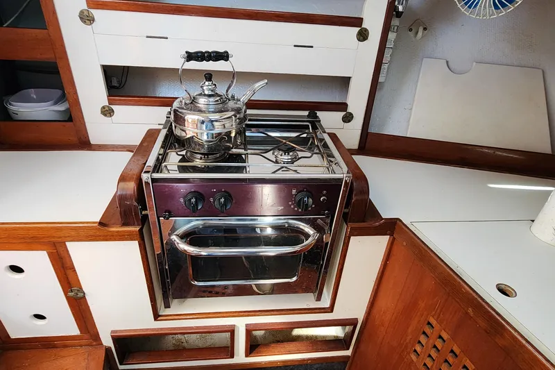 Slide: The Image of 1996 Tillotson-Pearson Motorsailer 32 kitchen with stove and kettle, featuring wood accents. - 54