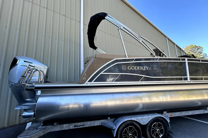 Slide: The Image of 2026 Godfrey Monaco 255 ULC pontoon boat on trailer, parked beside a building. - 2