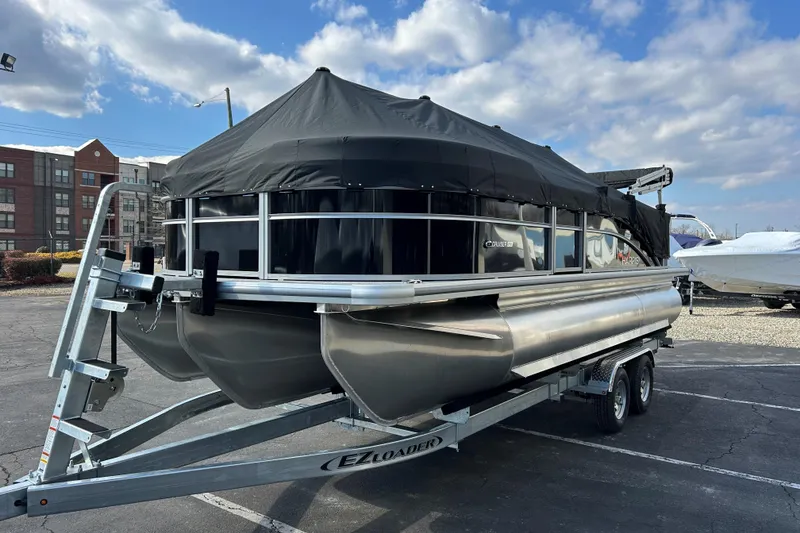 Slide: The Image of 2026 Harris Cruiser 210 pontoon boat on trailer, covered, parked outdoors under blue sky. - 22
