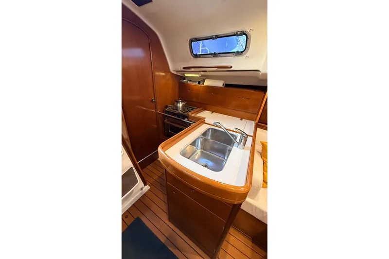 Slide: The Image of Interior of 2004 Beneteau First 36.7 yacht, featuring a compact kitchen with wooden cabinetry. - 10