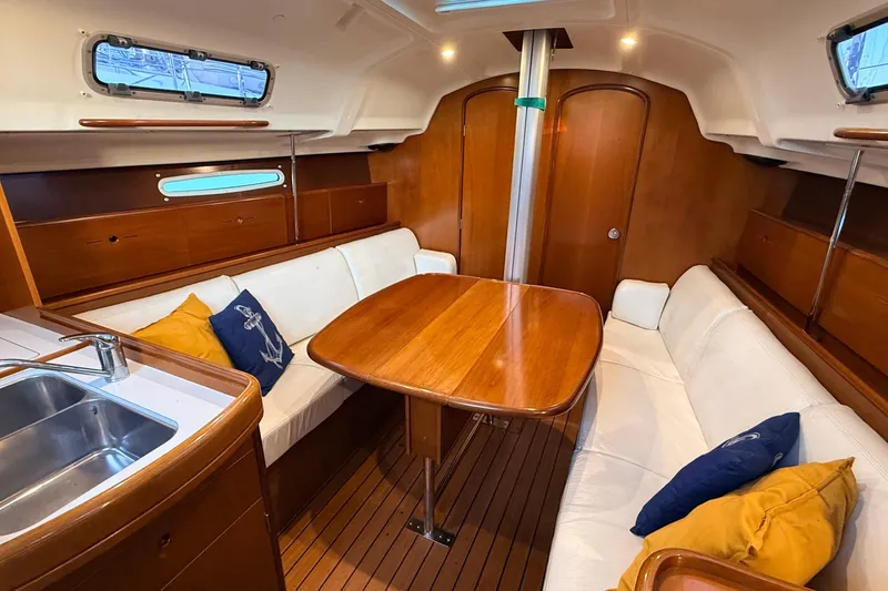 Slide: The Image of Interior of 2004 Beneteau First 36.7 sailboat with wooden table and white seating. - 2