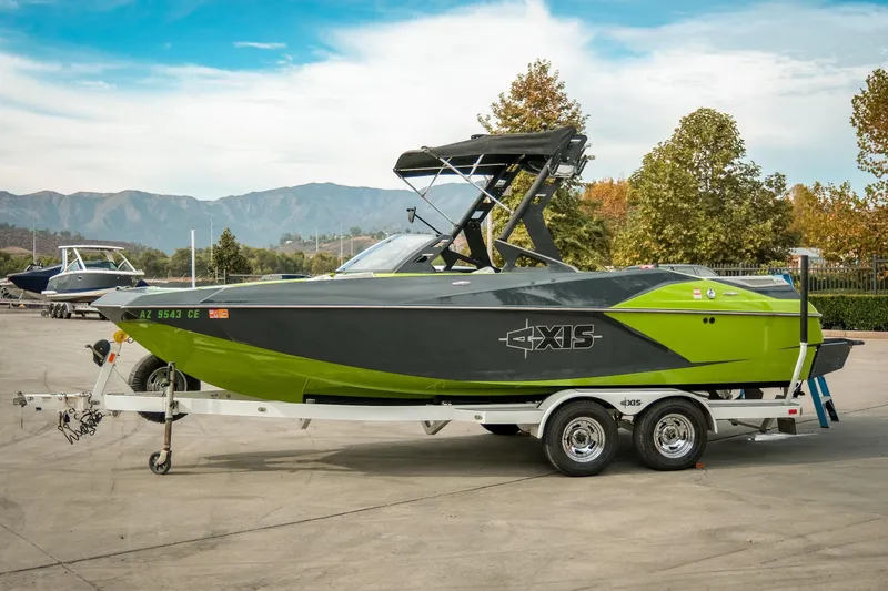 The Image of 2016 Axis A22 boat on trailer, green and black design, parked outdoors with scenic mountain backdrop. - 1