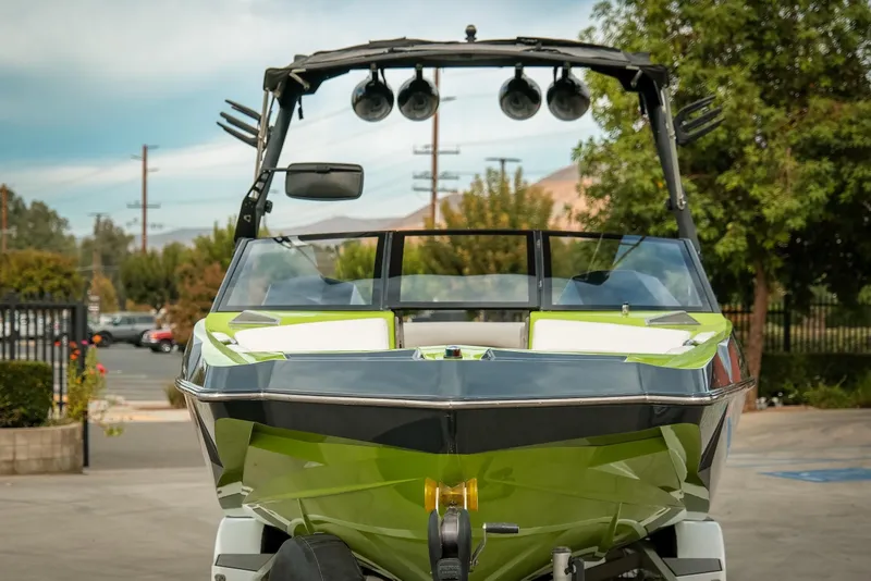 Slide: The Image of 2016 Axis A22 boat with green accents, parked outdoors, featuring a sleek design and tower speakers. - 2
