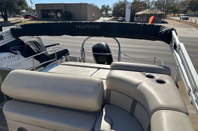 Slide: The Image of 2019 Harris Cruiser 230 boat with cushioned seating and covered motor, parked near a road. - 6