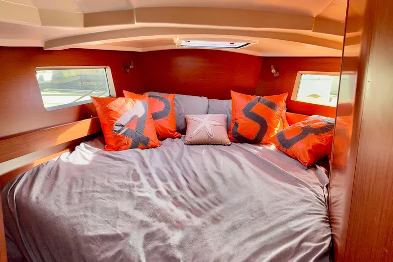Slide: The Image of 2019 Beneteau Oceanis 41.1 cabin with cozy bed, orange pillows, and wooden interior. - 44