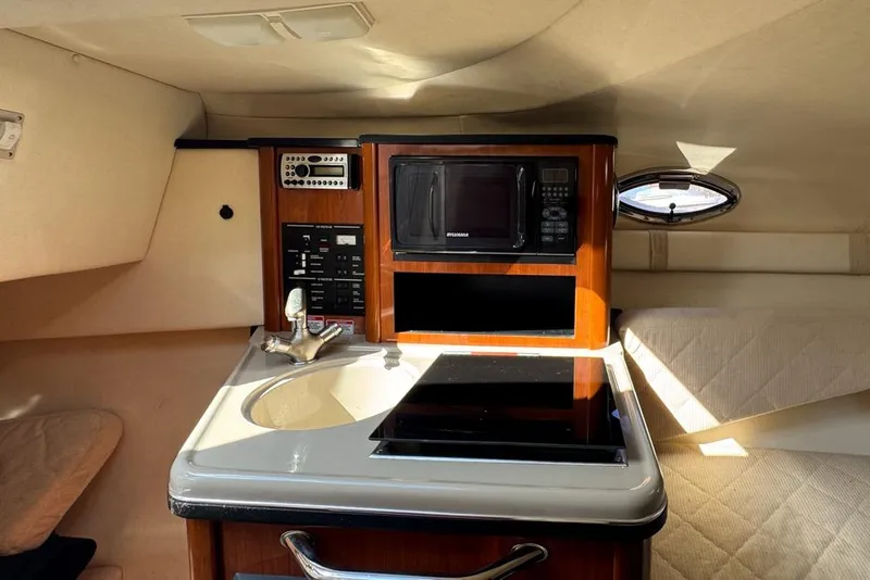 Slide: The Image of 2007 Sea Ray 240 Sundancer cabin with kitchenette, featuring sink, stove, and microwave. - 64