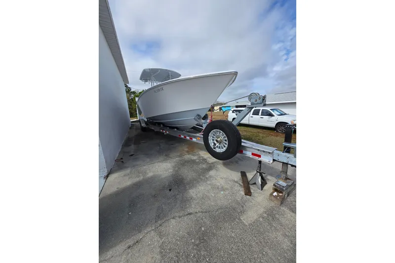 Slide: The Image of 2024 Contender 32 ST boat on trailer, parked beside a building under cloudy sky. - 32