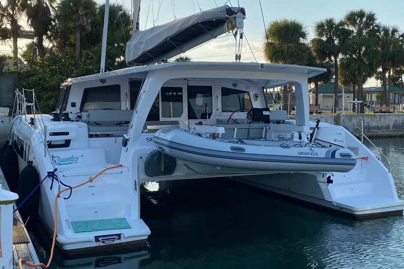 Slide: The Image of 2024 Seawind 1370 catamaran docked with inflatable boat, surrounded by palm trees. - 2