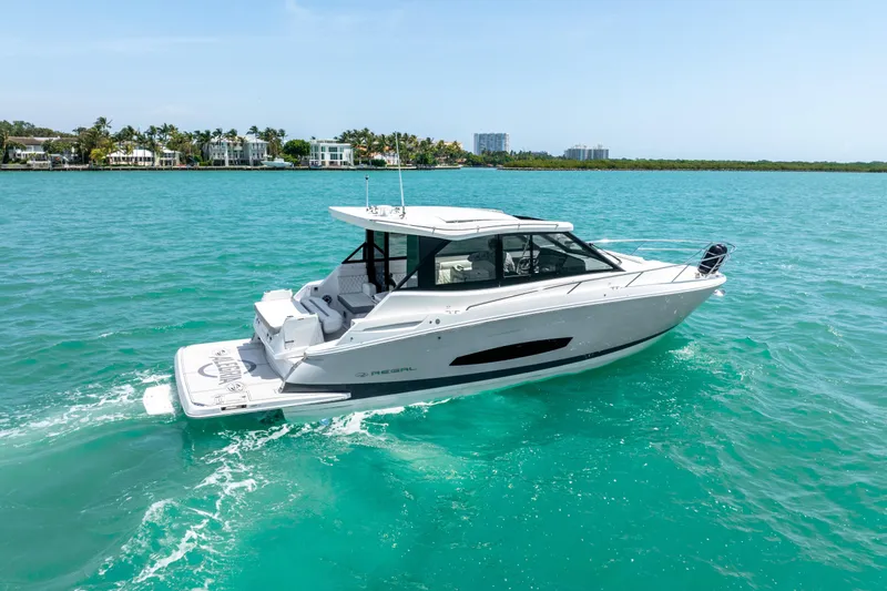 Slide: The Image of 2022 Regal 36 Grande Coupe cruising on turquoise waters near a coastal city. - 12