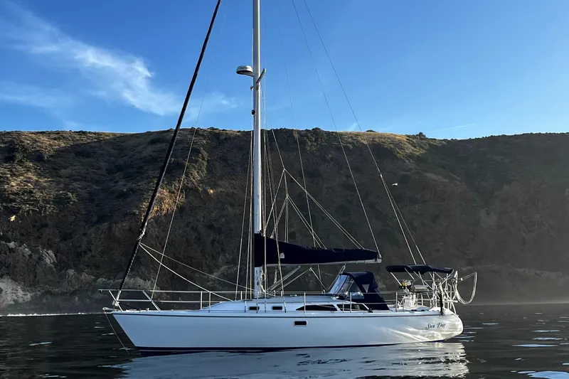 Slide: The Image of 1998 Catalina 36 MkII sailboat on calm water with rocky coastline backdrop. - 1