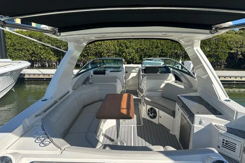 Slide: The Image of 2020 Sea Ray SLX 350 Outboard boat interior with seating and table, docked by greenery. - 10
