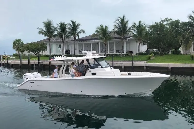 The Image of 2024 Pursuit S 358 Sport boat cruising near waterfront homes with palm trees. - 1