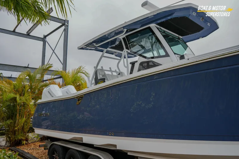 Slide: The Image of 2026 Blackfin 332 CC boat with blue hull, displayed outdoors near palm trees. - 11
