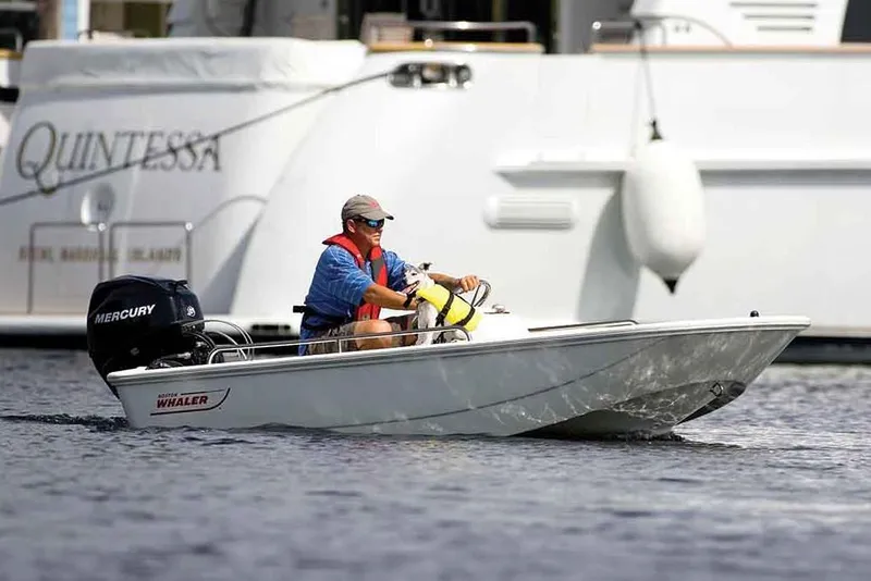 Slide: The Image of Manufacturer Provided Image: 2020 Boston Whaler 110 Sport boat cruising on water with a man at the helm. - 13