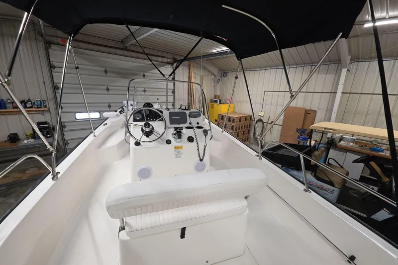 Slide: The Image of 2011 Boston Whaler 190 Montauk boat interior with steering console and canopy in a garage. - 7