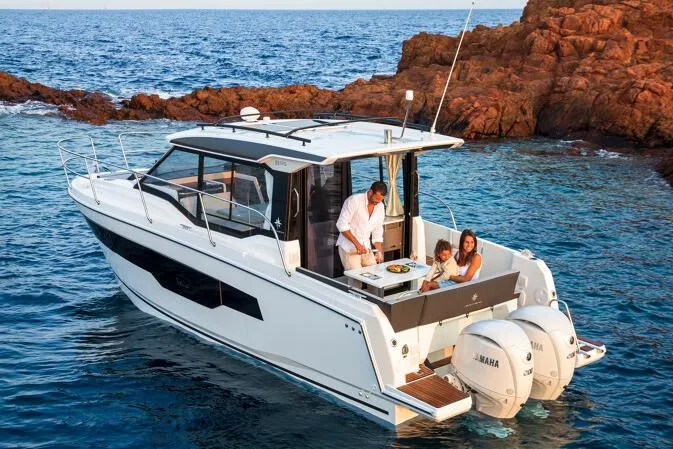 Slide: The Image of Manufacturer Provided Image: 2025 Jeanneau NC 895 Series 2 boat with family enjoying a meal on deck, near rocky coastline. - 4