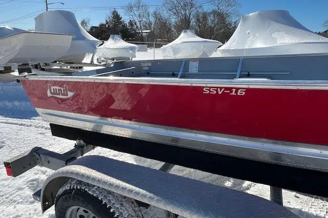 Slide: The Image of Red 2026 Lund SSV-16 boat on trailer, parked in snowy area with covered boats nearby. - 13