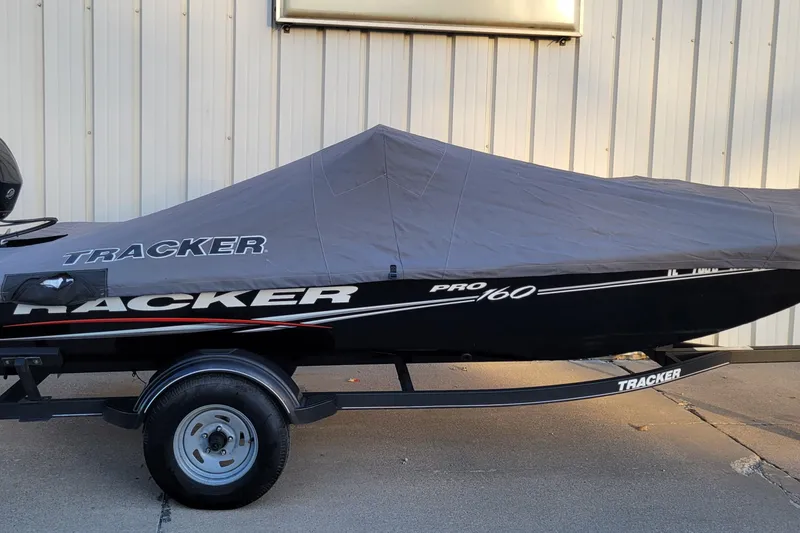 Slide: The Image of 2018 Bass Tracker Pro 16 boat covered, on trailer, parked by a building. - 7
