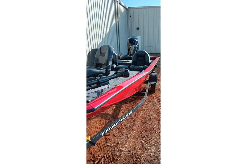 Slide: The Image of 2026 Tracker Pro Team 175 boat, red exterior, parked on dirt near a metal building. - 5