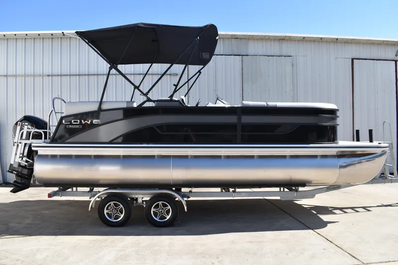 The Image of 2026 Lowe SS 230 WT pontoon boat with canopy on trailer, parked outside a warehouse. - 0