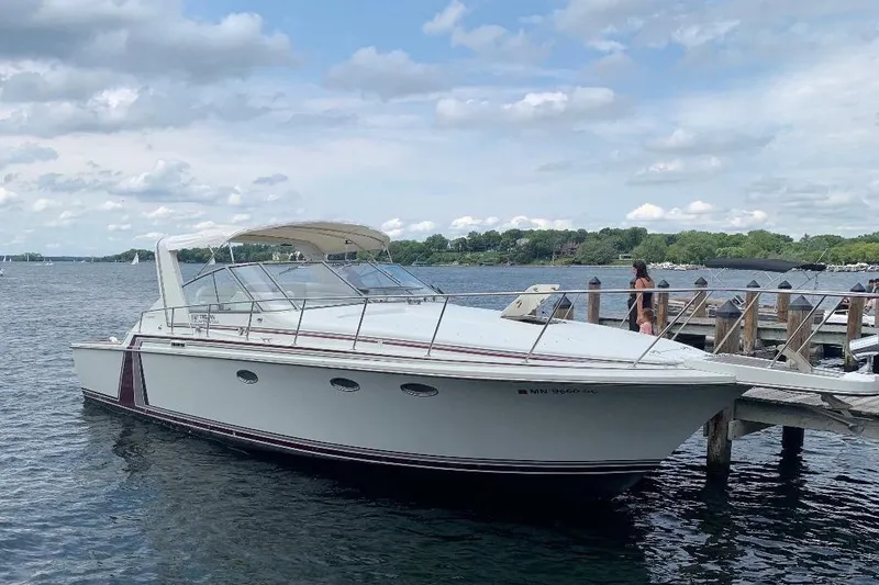 The Image of 1984 Trojan 11 Meter Express yacht docked on a serene lake under a cloudy sky. - 0