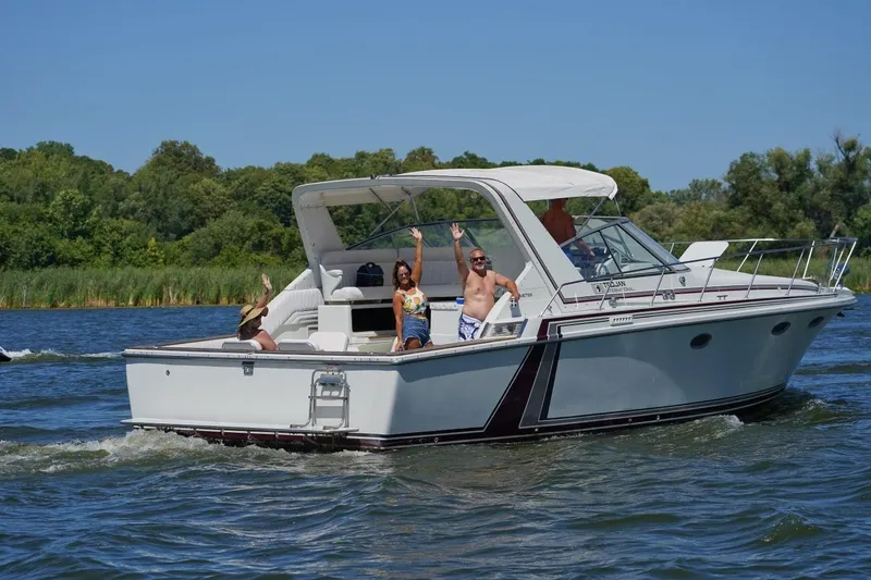 Slide: The Image of 1984 Trojan 11 Meter Express boat cruising with passengers waving on a sunny day. - 3