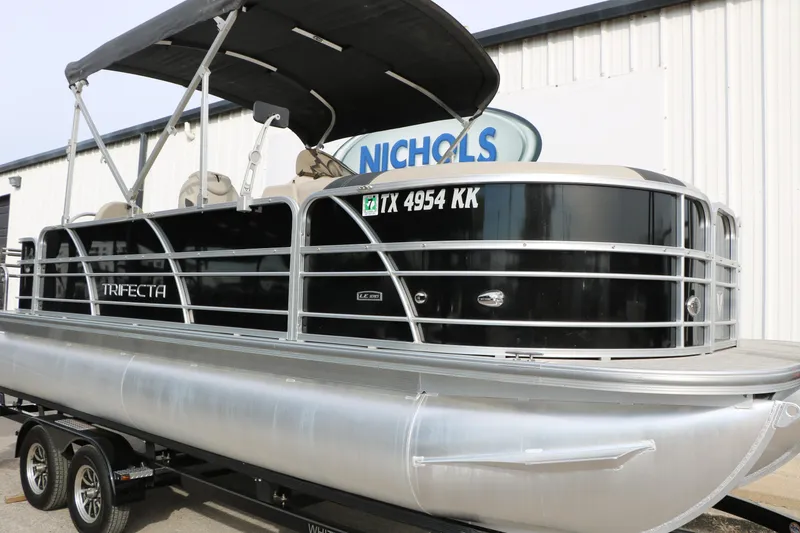 Slide: The Image of 2021 Trifecta 22 RFC pontoon boat on trailer, black and silver design, parked outside. - 7