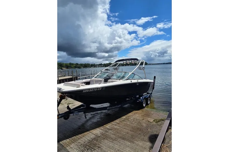 The Image of 2006 MasterCraft X-45 boat on trailer by a lake under cloudy sky. - 0