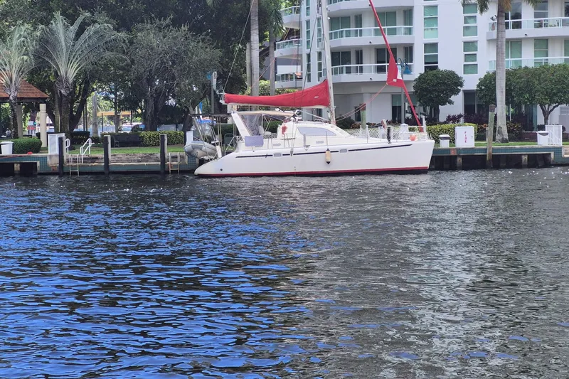 The Image of 2000 Leopard 38 catamaran docked at marina with red sail, surrounded by boats. - 0