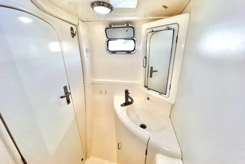 Slide: The Image of Compact bathroom in a 2000 Leopard 38 yacht with sink, mirror, and porthole window. - 92