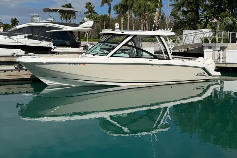 The Image of 2022 Boston Whaler 320 Vantage boat docked in a marina with clear water reflection. - 1