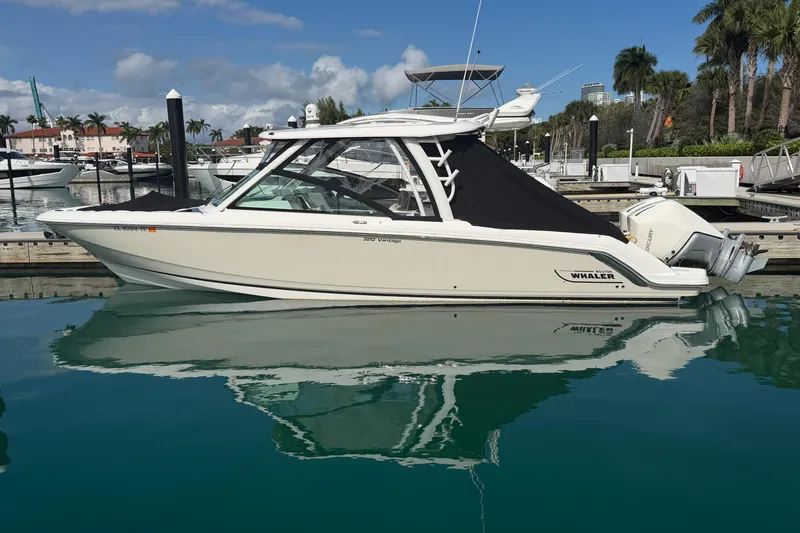 Slide: The Image of 2022 Boston Whaler 320 Vantage boat docked in a marina, reflecting on calm water. - 48