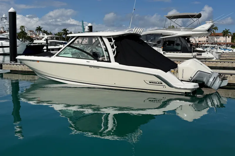 Slide: The Image of 2022 Boston Whaler 320 Vantage boat docked in a marina, reflecting on calm water. - 50