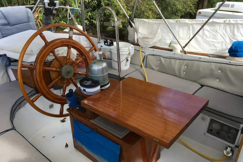 Slide: The Image of 1977 Ericson 36 C sailboat cockpit with wooden wheel and table, featuring comfortable seating. - 16