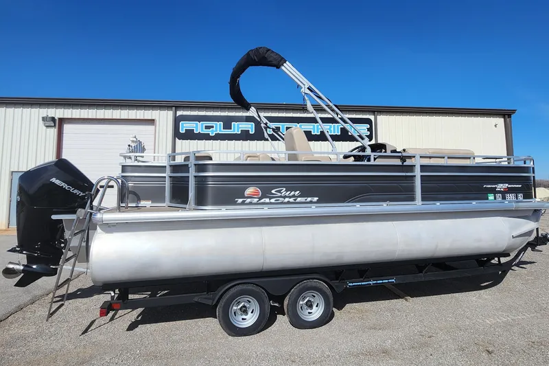 The Image of 2024 Sun Tracker Fishin' Barge 22 XP3 pontoon boat on trailer, parked outside. - 1