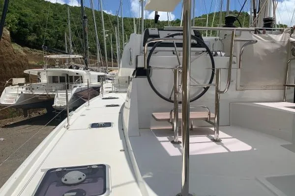 Slide: The Image of 2017 Lagoon 42 catamaran docked, showcasing deck and steering wheel, with lush greenery in background. - 54