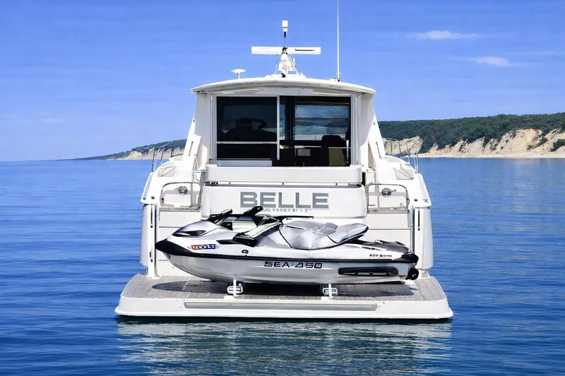 Slide: The Image of 2018 Cruisers Yachts 50 Cantius with jet ski on calm water, scenic coastal backdrop. - 5