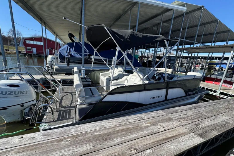 Slide: The Image of 2024 Crest Classic LX 220 SLRC pontoon boat docked under a covered marina. - 9