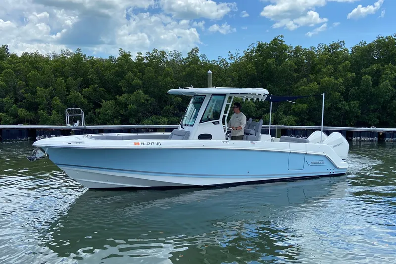 Slide: The Image of 2025 Boston Whaler 280 Outrage boat on calm water, surrounded by lush greenery. - 10